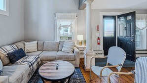 A living room with a sectional sofa, a round coffee table, and wicker chairs. - Historic Mill House near the Covered Bridge (Quechee)