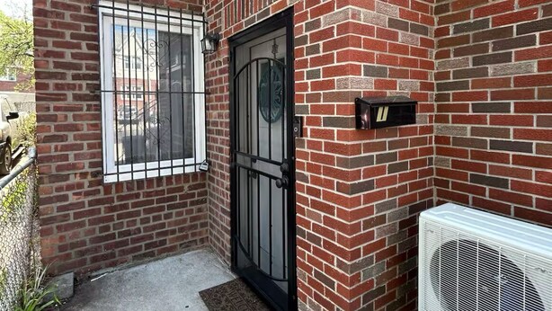 A brick building with a black gate, a small air conditioning unit, and a metal vent on the right side.