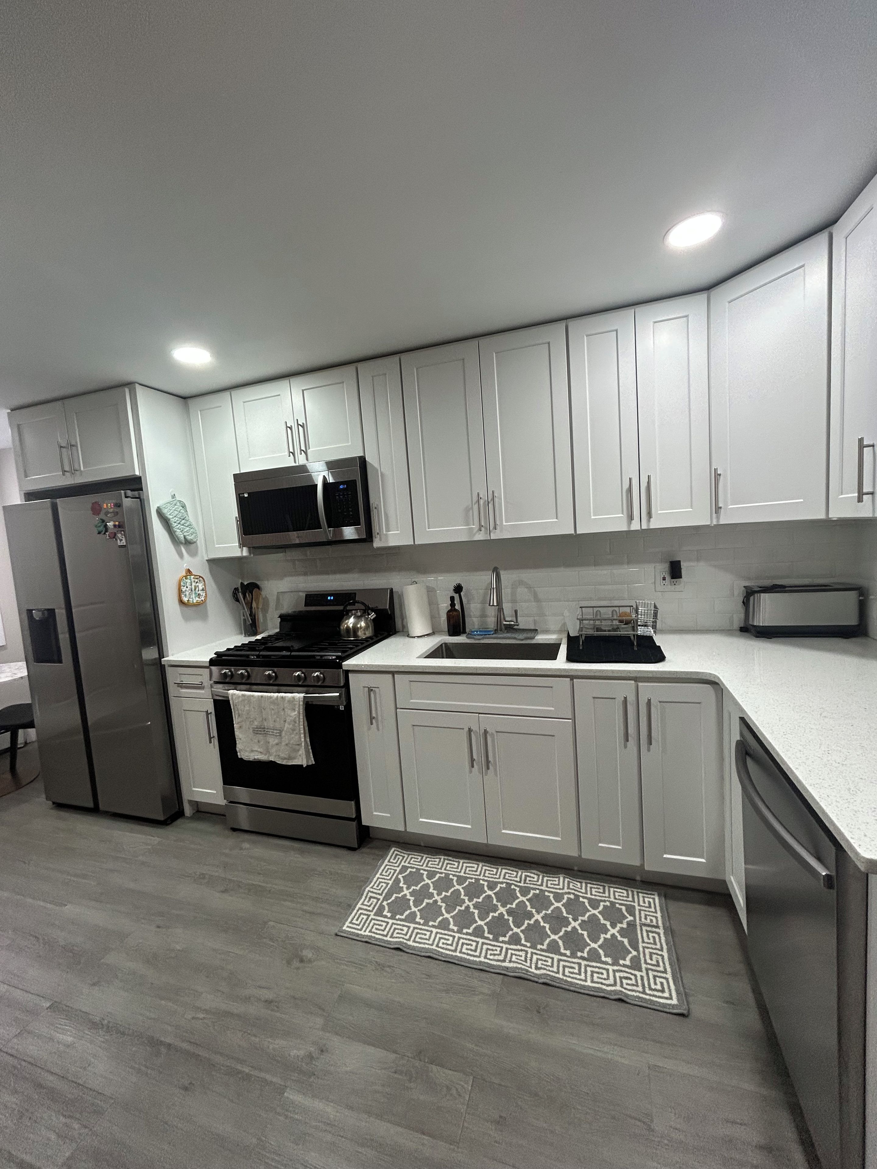 Una cocina moderna con armarios blancos, electrodomésticos de acero inoxidable y una alfombra estampada.