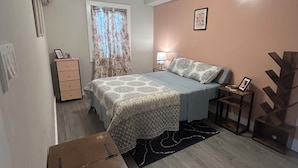 A bedroom with a bed, bedside table, lamp, and a decorative plant.