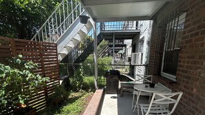 An outdoor patio area with a covered seating area, a metal staircase, and a brick building in the background.