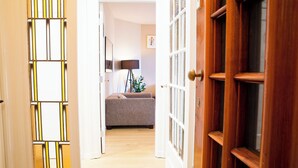 Un couloir avec une porte en bois, une porte en verre avec un cadre jaune et blanc, et un canapé gris en arrière-plan.