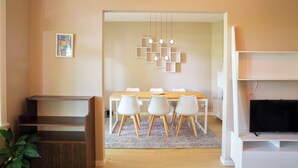 Un salon moderne avec une table à manger en bois, des chaises blanches, un téléviseur et un luminaire décoratif.