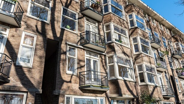 Un immeuble en briques à plusieurs étages, doté de nombreux balcons, de grandes fenêtres et d’une porte bien visible.