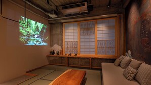 A traditional Japanese room with tatami flooring, a low wooden table, a sofa with patterned cushions, a projection screen displaying a forest scene, and a shoji screen with intricate patterns. - Walking distance from Asakusa｜ Moon presentation only in January and February｜ Rice cooking and sake｜ Private use of one floor｜ Couple/Family｜ 36 square meters｜ Max. 4 persons (Matsugaya, Taito City)