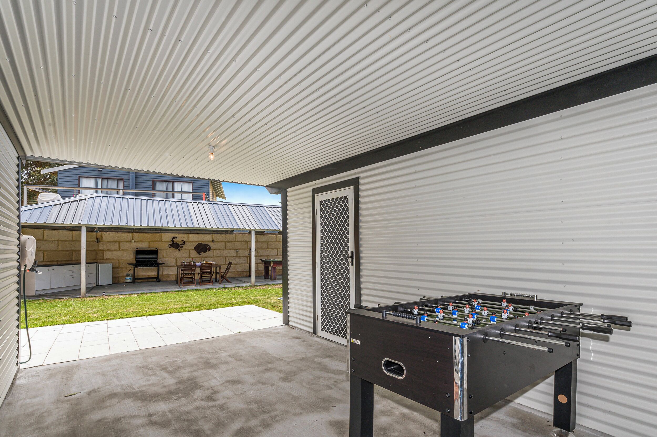 An outdoor patio area with a foosball table, a barbecue grill, and a covered seating area.