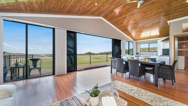 Un vaste espace de vie avec une grande porte-fenêtre coulissante donnant sur un balcon, un coin repas avec une table et des chaises, et un ventilateur de plafond.