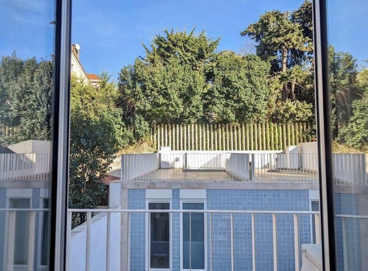 A modern building with a balcony and a view of trees and a fence.