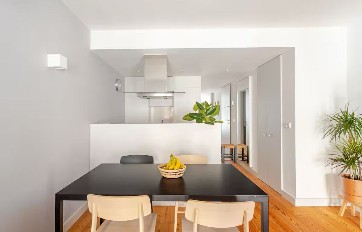 Une cuisine moderne avec des meubles blancs, un plan de travail noir et un îlot central agrémenté d’une plante.