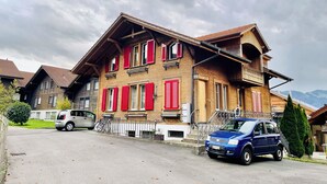 Une maison à deux étages avec des volets rouges, un balcon et une voiture garée devant.