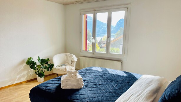Une chambre à coucher avec un lit, une chaise, une fenêtre et une plante en pot.