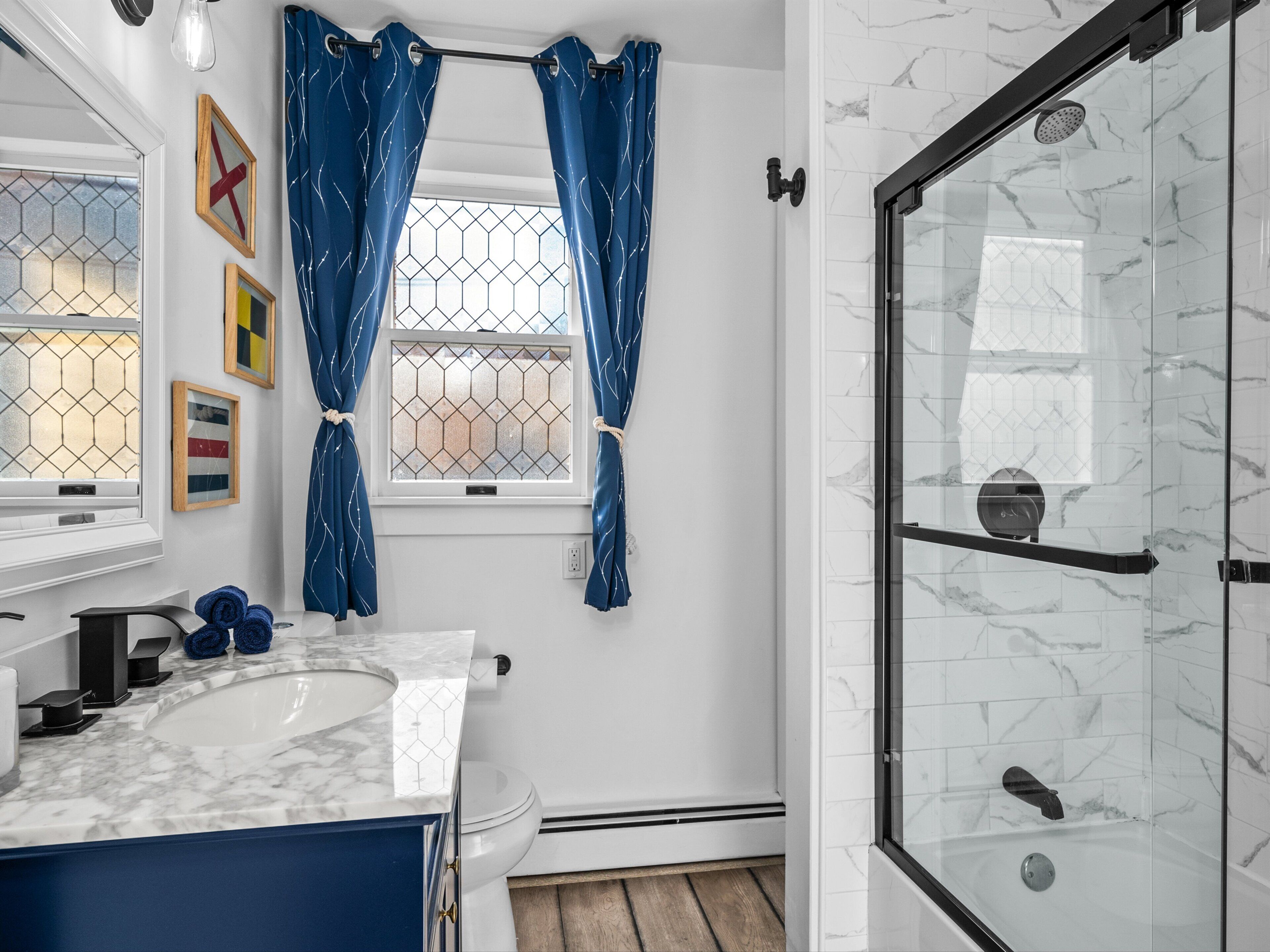 Ein modernes Badezimmer mit einem мраморным Waschbecken, einer Duschkabine aus Glas und einem Fenster mit blauen Vorhängen.