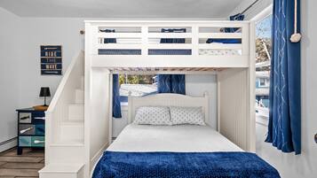 A bunk bed with a white frame and blue bedding, a small table with a lamp, and a 'Ride the Wave' sign on the wall.