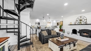 Un salon moderne avec un escalier en colimaçon noir, une cheminée et une cuisine en arrière-plan.