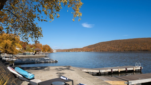 Une jetée au bord du lac, avec des chaises longues et une petite table, entourée d’un feuillage automnal et sous un ciel dégagé.