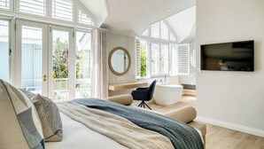Ein modernes Schlafzimmer mit einem großen Bett, einer Sitzecke mit einem Sessel, einem runden Spiegel und einem Fernseher an der Wand.