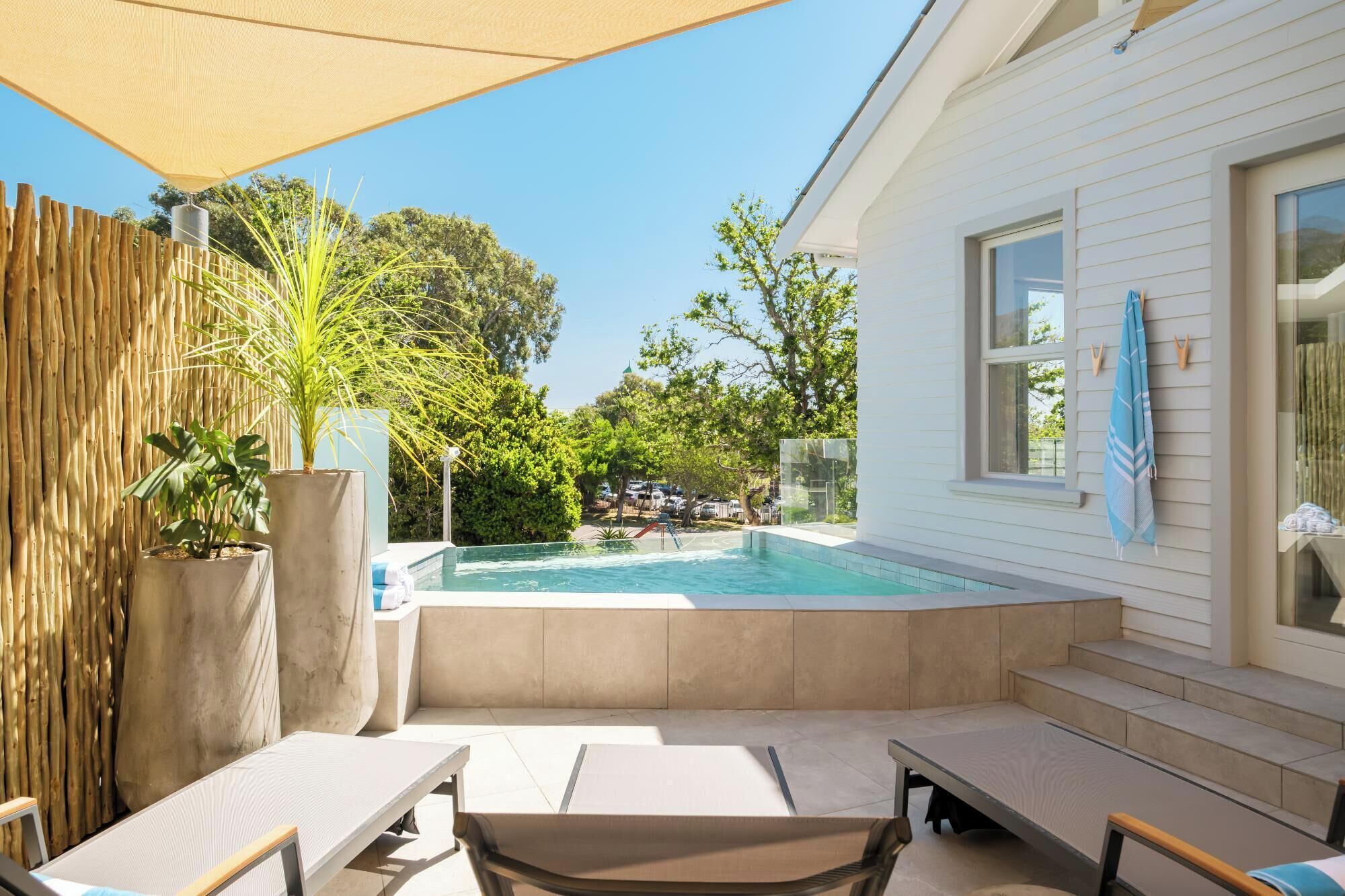 A backyard with a swimming pool, outdoor seating, and a house with a large window.