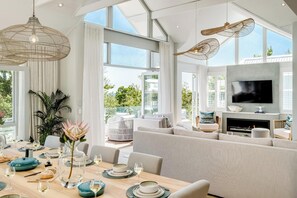 A modern living room with a large TV, comfortable seating, and a dining area with a table set for a meal. - 6bed Villa by Camps Bay Beach Seven the Drive (Cape Town)