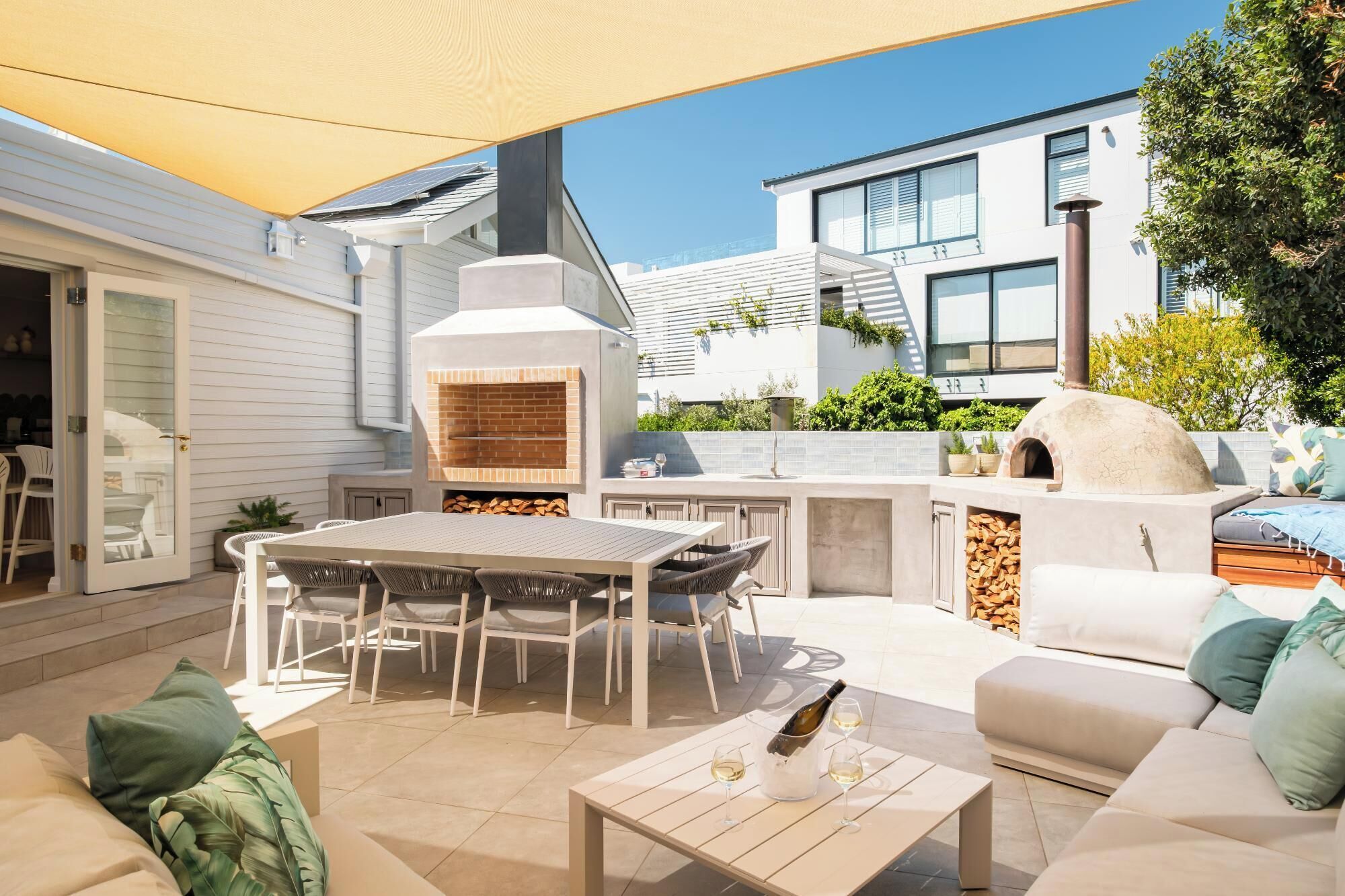 An outdoor patio with a built-in pizza oven, a dining table with chairs, and a seating area with cushions.