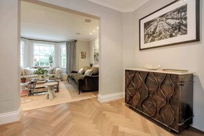A spacious living room with a large window, a sofa, a coffee table, and a decorative cabinet. - Gorgeous 3 bed House in Sloane Square (London)