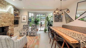 A modern dining area with a long wooden table, patterned chairs, and a brick wall with a fireplace. - Gorgeous 3 bed House in Sloane Square (London)