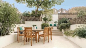 A patio with a round table and six wooden chairs, surrounded by white walls and greenery. - Gorgeous 3 bed House in Sloane Square (London)