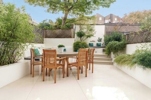 A patio with a round table and wooden chairs, surrounded by white walls and potted plants. - Gorgeous 3 bed House in Sloane Square (London)