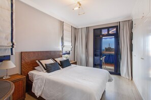 Ein Hotelzimmer mit einem großen Bett, einem Holzkopfende, einem Nachttisch mit Lampe, Blick durch eine Glastür nach draußen und einem Balkon.