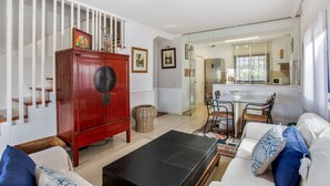 Ein Wohnzimmer mit einer Couch, einem Couchtisch, einem roten Schrank und einer Küchenzeile mit Esstisch und Stühlen.