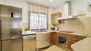 Eine moderne Küche mit Edelstahlgeräten, Holzschränken und einem Fenster mit Jalousien.