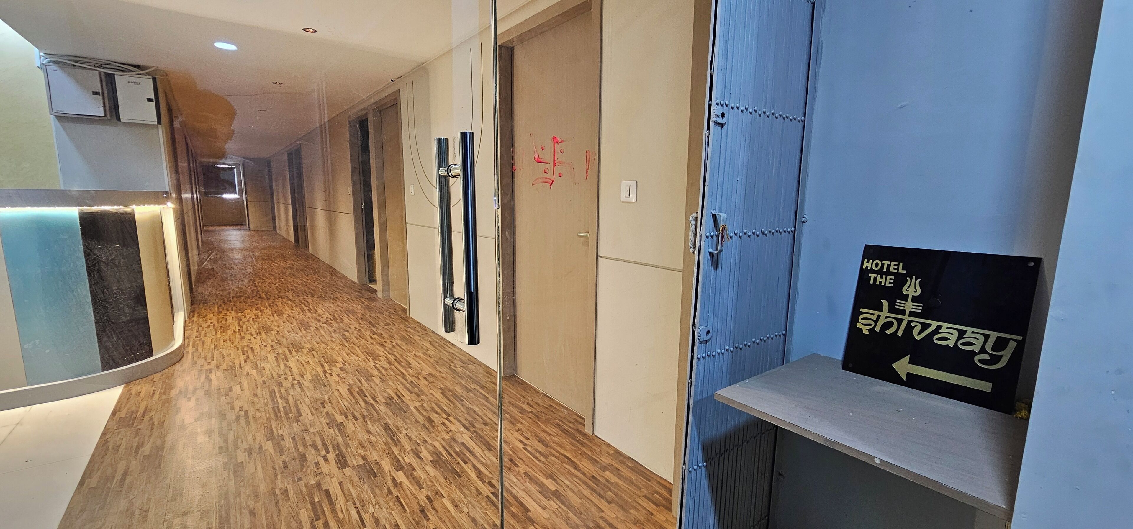 A hotel hallway with wooden flooring, a glass partition, and a sign indicating the direction to the hotel.