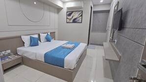 Una habitación de hotel moderna con una cama grande, una mesita de noche con botellas de agua, un televisor de pantalla plana y un equipo de aire acondicionado.
