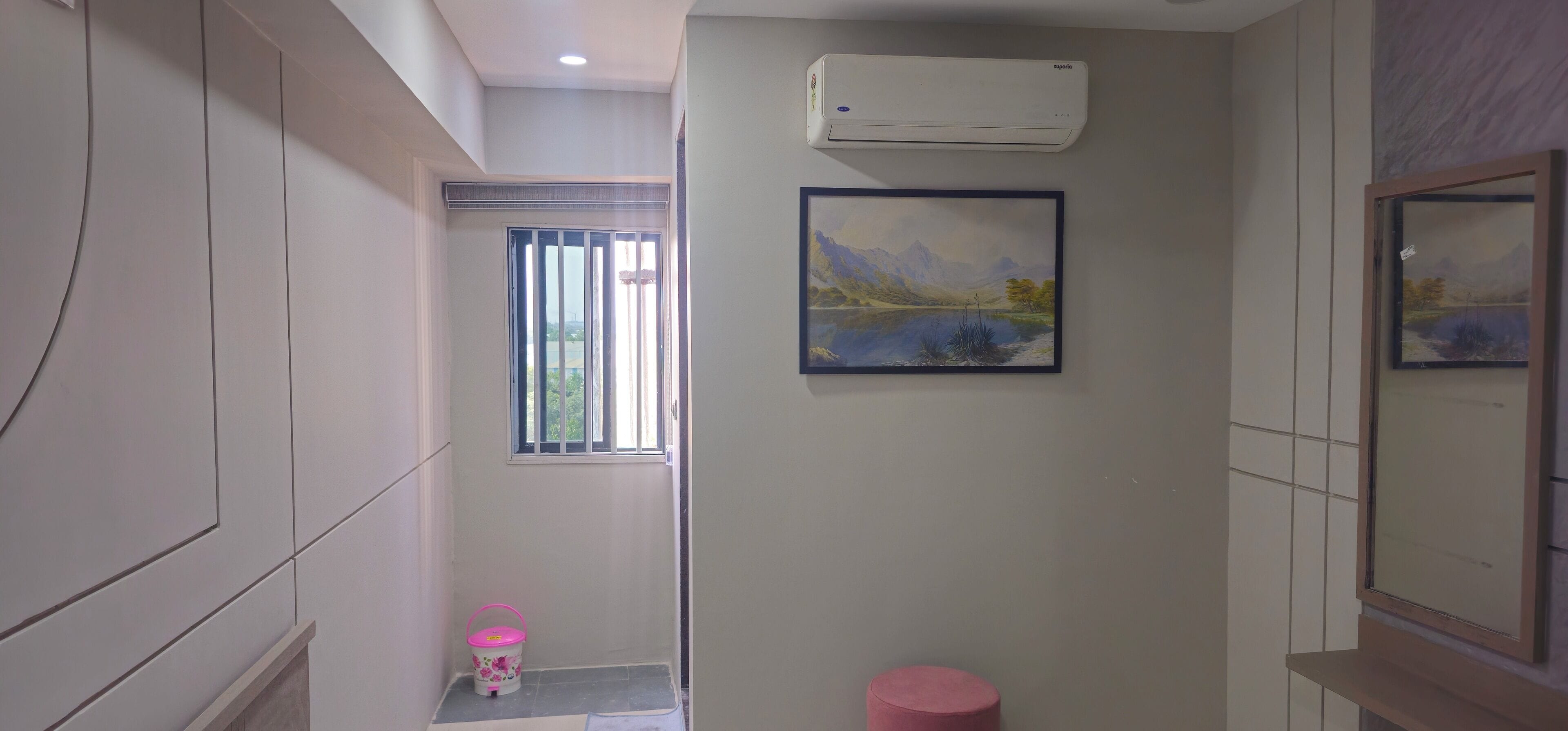 A bathroom with a window, a painting, a pink bucket, and a white air conditioner.