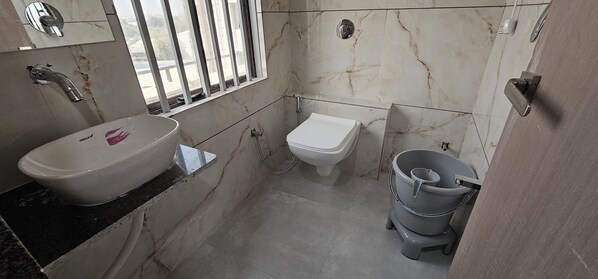 A bathroom with a white sink, toilet, and a grey bucket. - Hotel The Shivay (Ahmedabad)