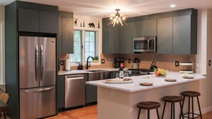 A modern kitchen with stainless steel appliances, a central island with stools, and a window with a view of trees. - 4BR Mtn Retreat w/ Hot Tub, Game Rm & 2 Kitchens – 15 Mins to North Conway! (Conway)