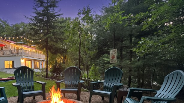 A fire pit surrounded by Adirondack chairs in a gravel area with trees and a building in the background. - 4BR Mtn Retreat w/ Hot Tub, Game Rm & 2 Kitchens – 15 Mins to North Conway! (Conway)