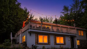 A two-story house with a balcony, large windows, and string lights. - 4BR Mtn Retreat w/ Hot Tub, Game Rm & 2 Kitchens – 15 Mins to North Conway! (Conway)