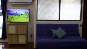 A room with a blue sofa, a television on a wooden cabinet, and a patterned window. - Oasis studio - Great location (Vientiane)