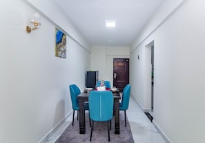 A narrow hallway with a dining table set for four, flanked by two blue chairs, leading to a dark wooden door. - Luxurious Nairobi Apartment With City and Garden Views (Nairobi)