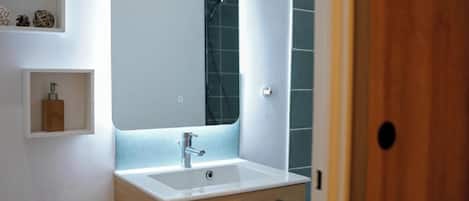 A modern bathroom with a large mirror, a white sink, and a wooden cabinet.