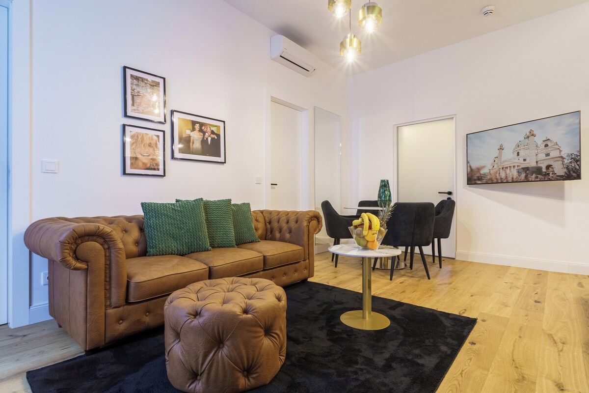 A living room with a brown leather sofa, a matching ottoman, a round coffee table, and a dining area with a table and chairs.