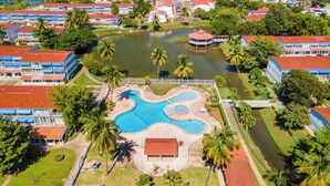 An aerial view of a resort with a central swimming pool, surrounded by palm trees and a body of water. - Relaxing Beach Villa in Dorado (Dorado)