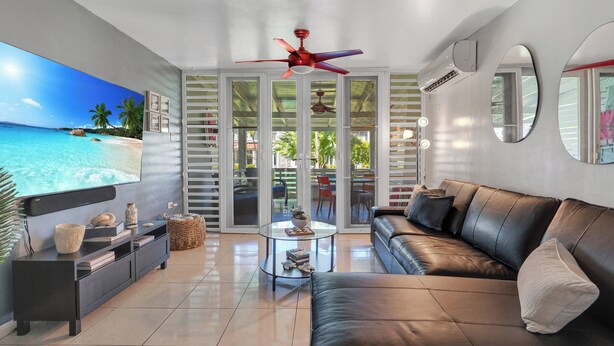A modern living room with a large flat-screen TV, a leather sofa, a glass coffee table, and a ceiling fan. - Relaxing Beach Villa in Dorado (Dorado)