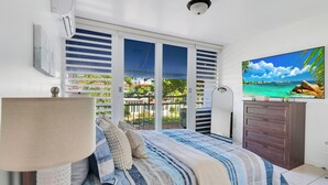 A bedroom with a bed, a dresser, a TV, and a balcony with a view of the ocean. - Relaxing Beach Villa in Dorado (Dorado)