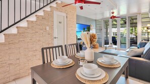 A dining area with a wooden table set for four, a staircase, and a living area with a sofa and a TV. - Relaxing Beach Villa in Dorado (Dorado)