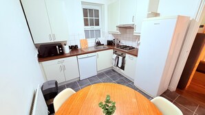 Une cuisine moderne avec des armoires blanches, un plan de travail en bois, un four encastré et une table à manger avec des chaises.