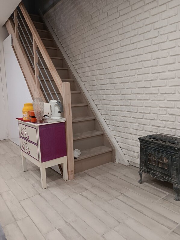 A staircase with a white brick wall, a wooden staircase railing, a white cabinet with drawers, and a black metal object on the floor.