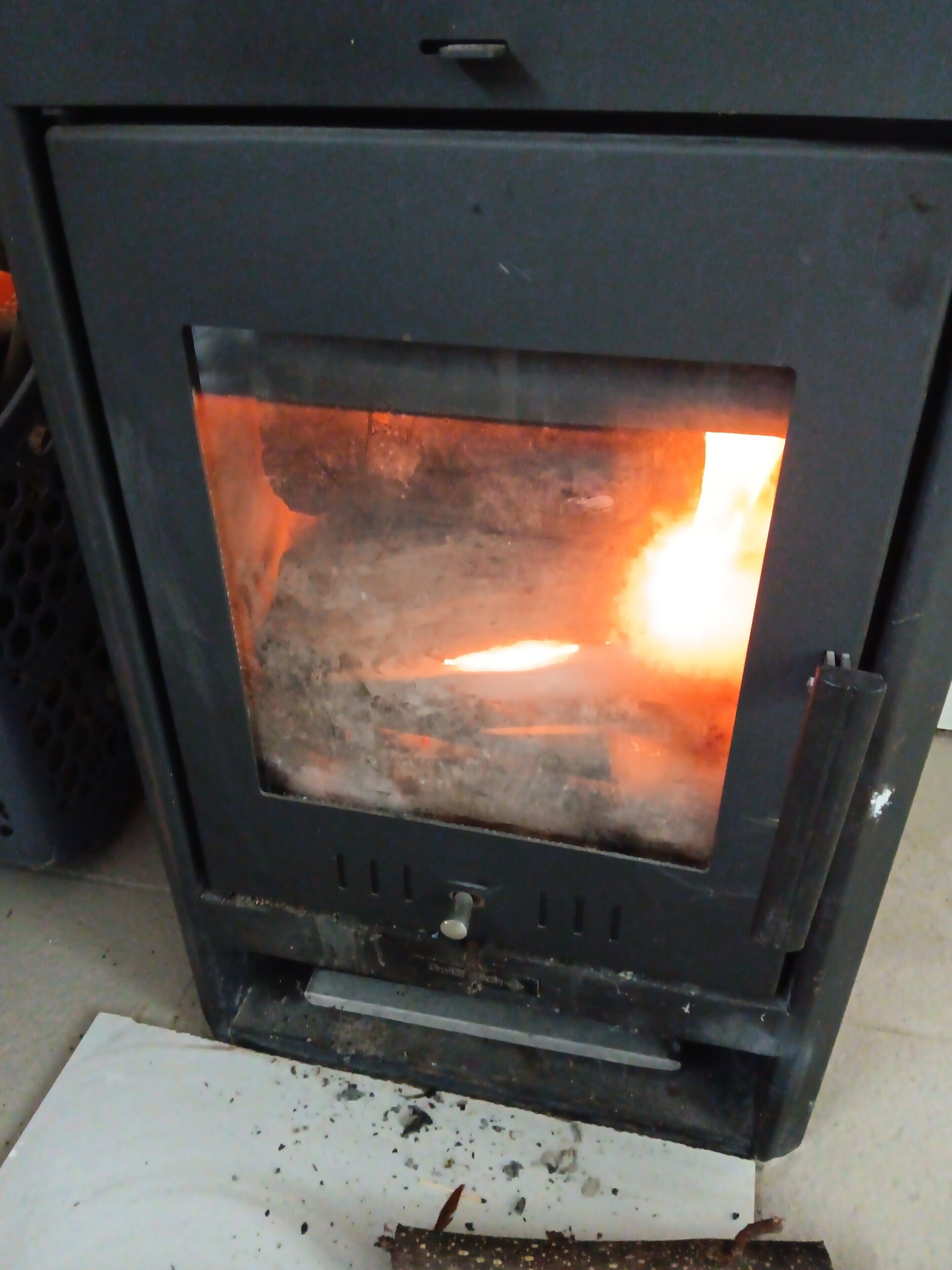 Ein Kaminofen mit sichtbaren Flammen, einem Einstellknopf und einem Abluftventil.