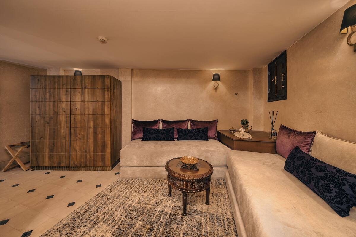 A spacious bedroom with a large bed, a wooden wardrobe, a round coffee table, and a patterned rug.