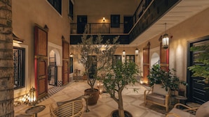 A spacious lobby with a checkered floor, potted plants, wicker furniture, and a staircase connecting two levels. - Riad Dar Yuba  (Marrakech)